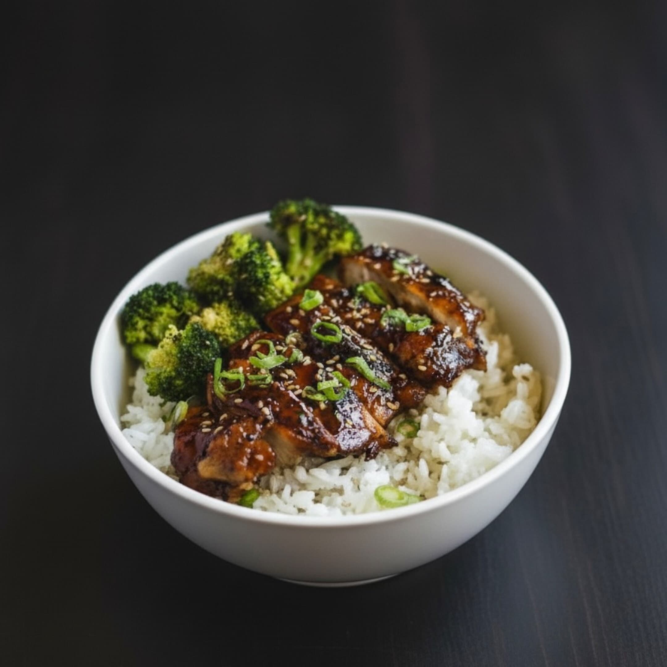Teriyaki chicken rice bowl with broccoli, scallion and sesame, plated dark